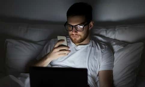 Man on phone and laptop in bedroom 