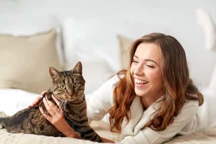 image of woman holding cat on a bed. 