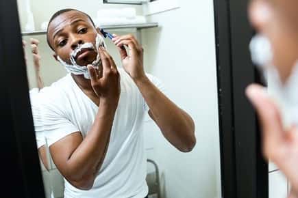 Image of a man shaving his beard in the mirror with shaving cream.