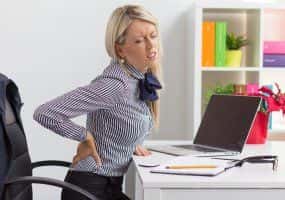 image of woman in pain holding her back while sitting at work
