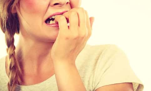 A closeup image of a woman who is anxiously biting her nails. 