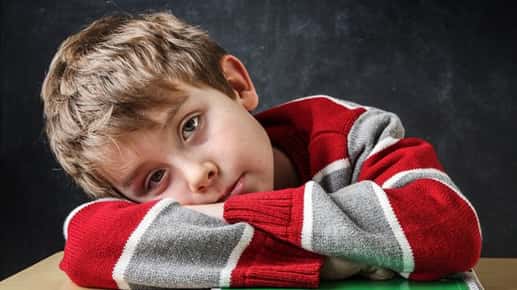 Image of a boy laying his head on his arms while sitting at a desk.