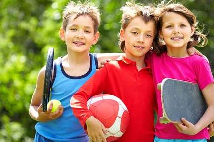 An image of a group of three elementary school-aged children, each holding a piece of sports equipment. 