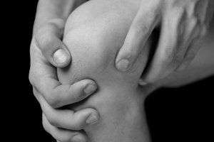 close up image of two hands holding a knee in pain