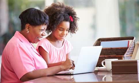 An image of a mother and young daughter smiling while looking at a laptop screen. 