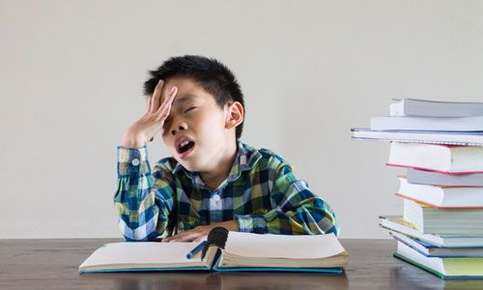 Image of a child who has a book open in front of him and appears to be frustrated and tired. 