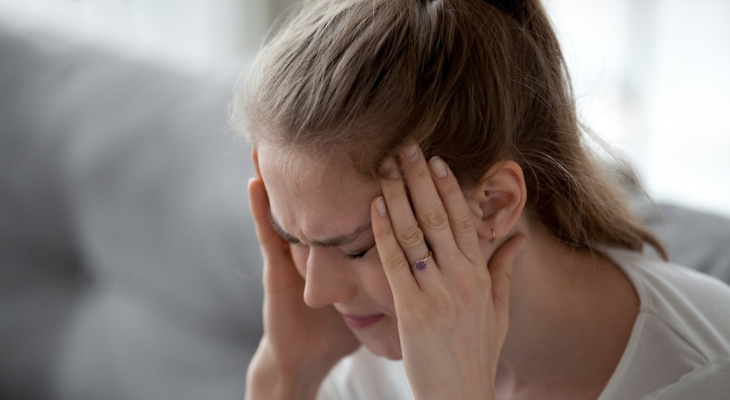 Woman in pain holds the sides of her head.