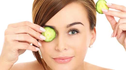 Image of a woman holding a cucumber slice to one of her eyes.
