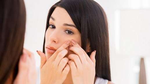 Image of a woman closely examining her face in a mirror.