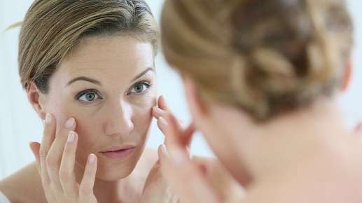 Image of an older woman examining her face in a mirror.