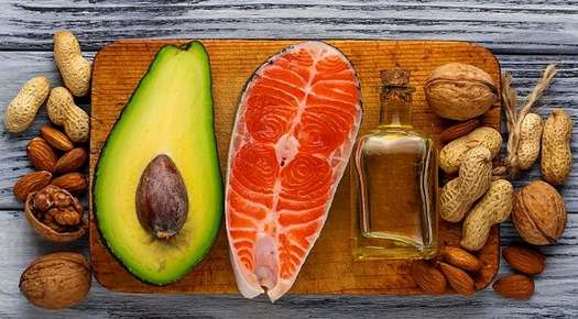 Image of an avocado, nuts, and oil laid out on a cutting board. 