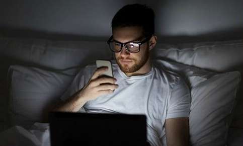 Man on phone and laptop in bedroom 