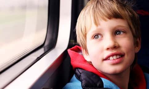 An image of a child with autism, who is riding on a train looking out the window. 