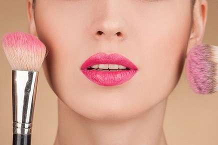 Image of a person wearing lipstick and holding a brush blush.