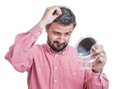 Image of a man looking at his white hair in a mirror.