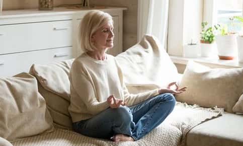 Older woman meditating on couch at home
