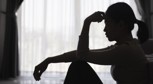 Stressed woman sitting in a shadowy room.