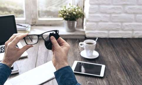 An image from the view of someone sitting at their desk while cleaning their classes with a soft cloth. 