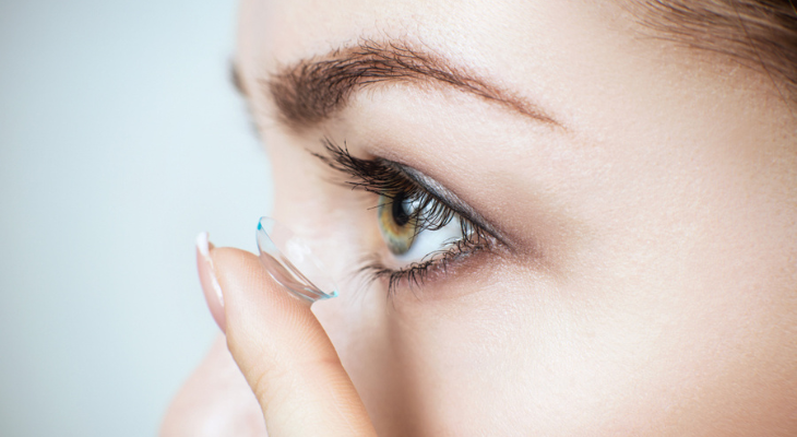 Woman holds contact lens on her finger.