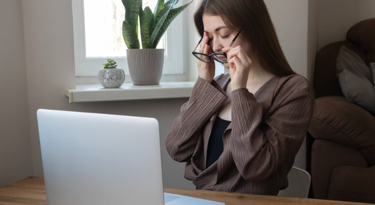 Woman with glasses rubs her sore eye.