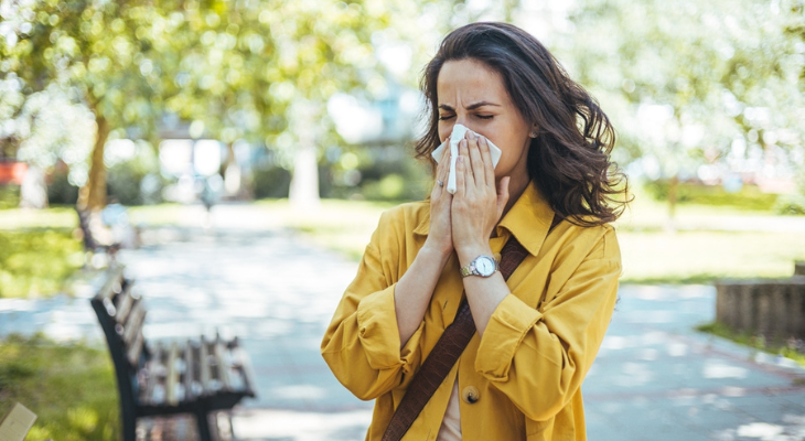 Woman with seasonal allergies blows her nose in the park.