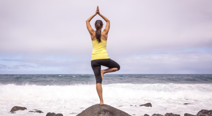 Woman doing tree pose at beach