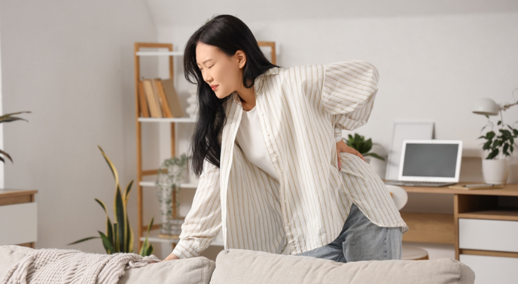 Asian woman holds her back in pain.