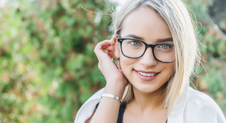 Woman wearing glasses touches her ear.