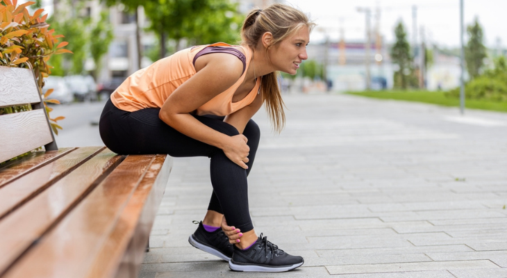 Woman sits on a bench holding her leg.