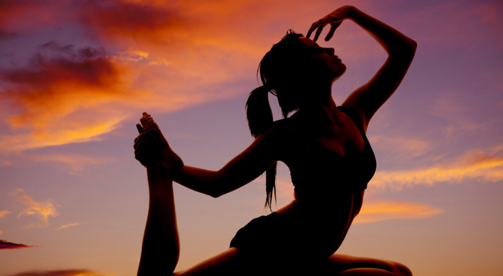 Woman does yoga on the beach during sunset.