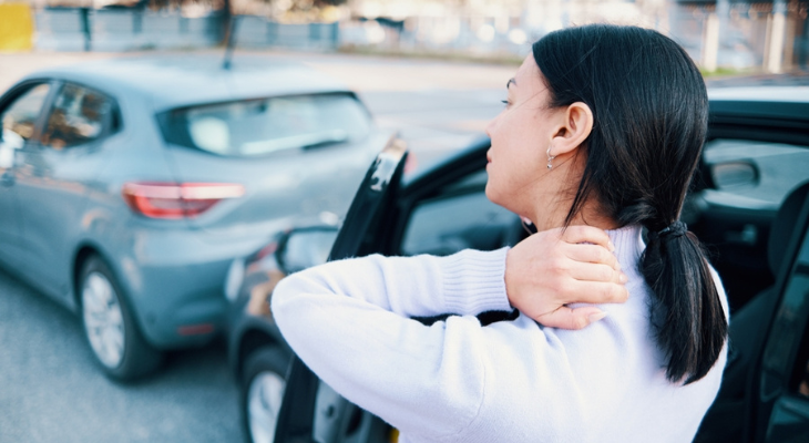 Woman holds her neck while standing next to car.