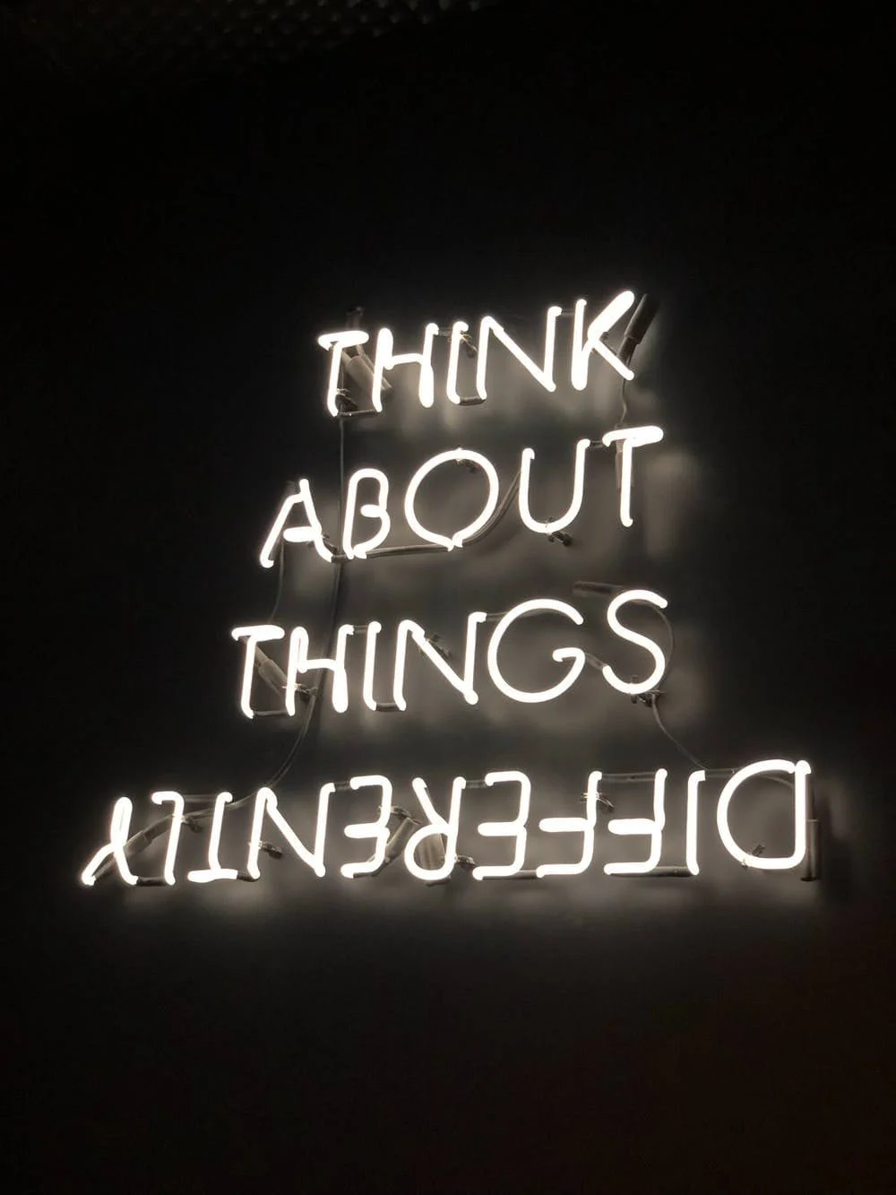 A black sign with neon type that says, "Think About Things Differently". Differently is hanging upside down.