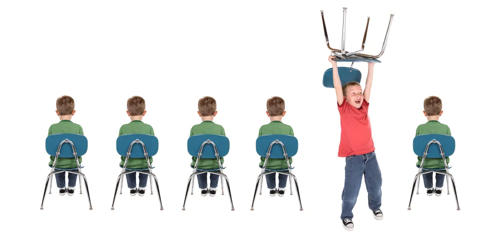 Child holding chair over his head while other children sit