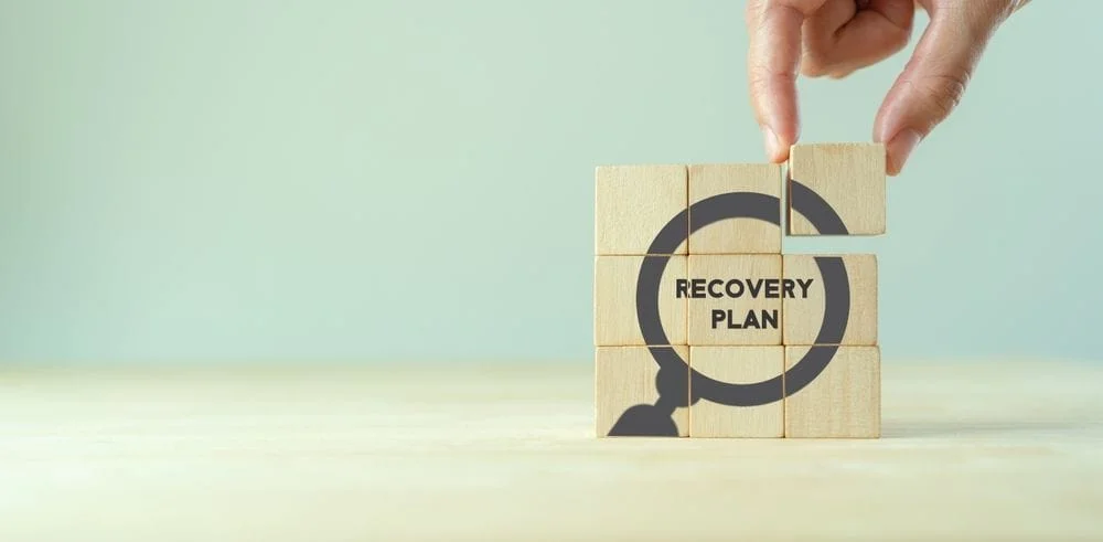 Hand putting word blocks together "Recovery Plan"