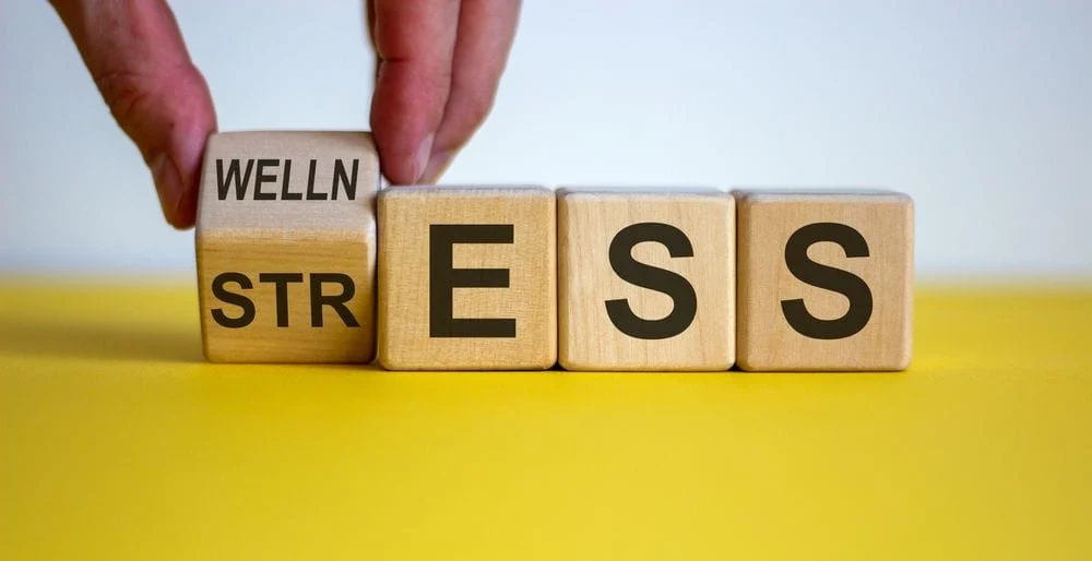 Wooden blocks spelling out STRESS being turned to WELLNESS
