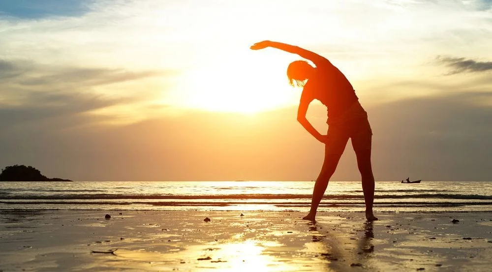 woman stretching at sunset on the beach after chiropractic care to relieve her back pain
