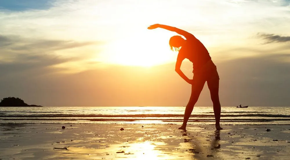 woman stretching at sunset on the beach after chiropractic care to relieve her back pain