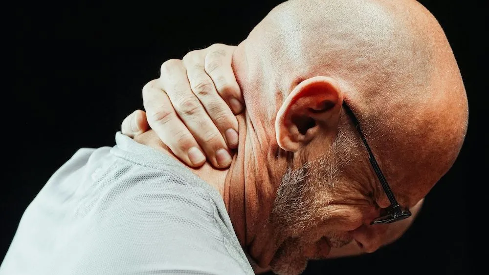 Bald man gripping his neck in pain after motor vehicle accident