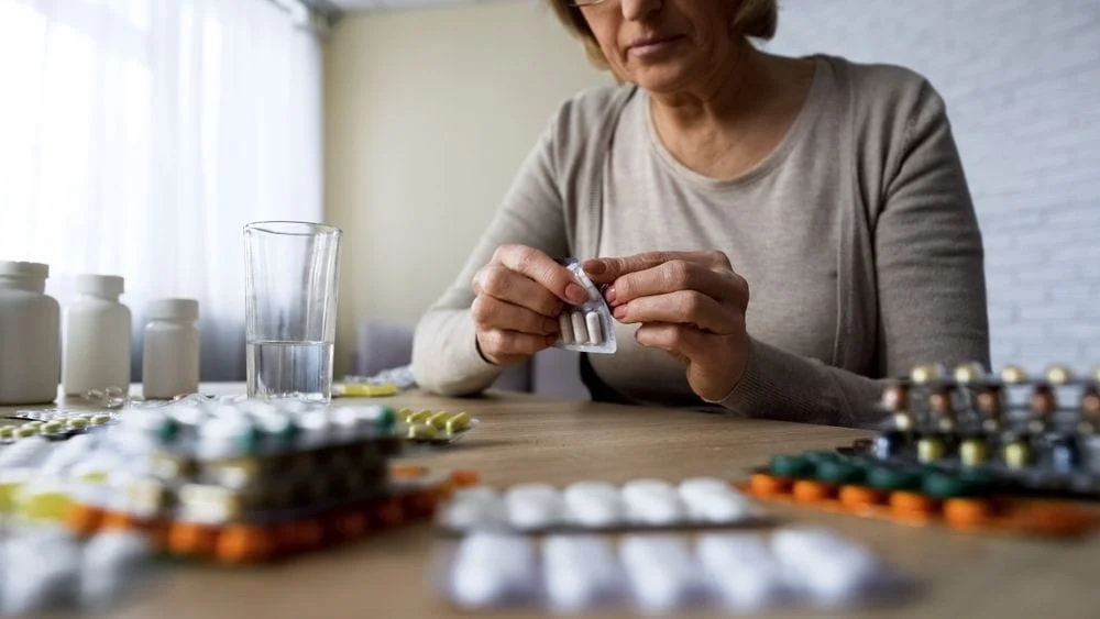 Woman sitting at a kitchen table opening pills in blister packs