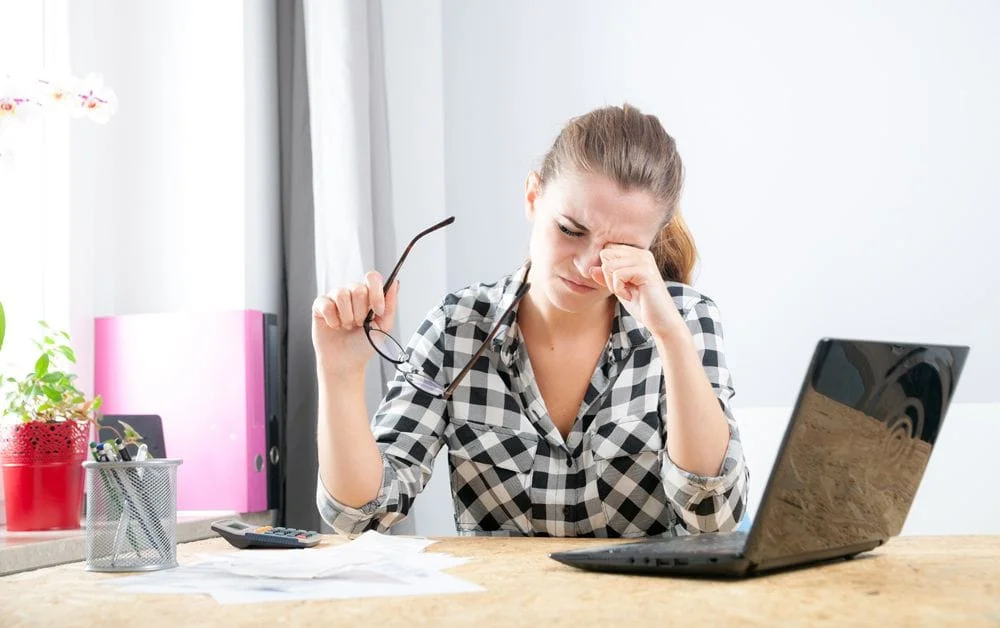 woman rubbing her eyes from digital eye strain from working on her laptop