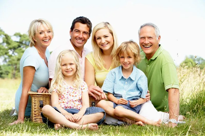 family smiling sitting in grass outside, parents, two kids, and grandparents, family dentistry Melrose, MA