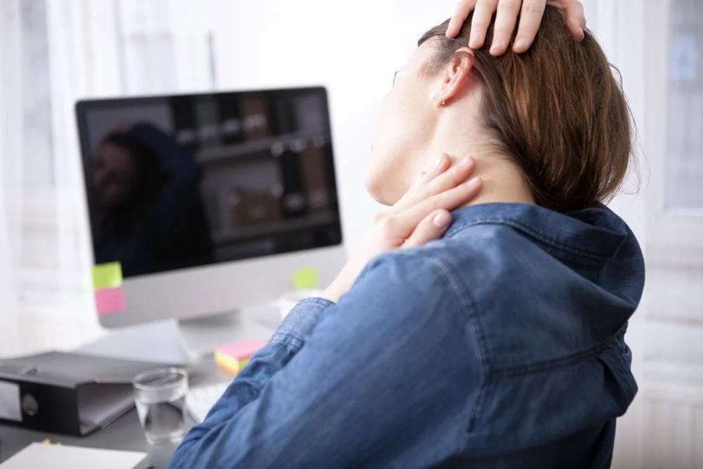 woman holding her neck while sitting at her computer from pain from tech neck