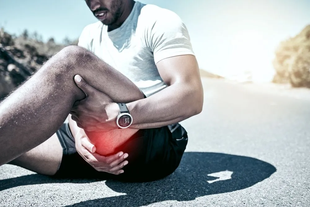 Man sitting on the ground holding hamstring in pain