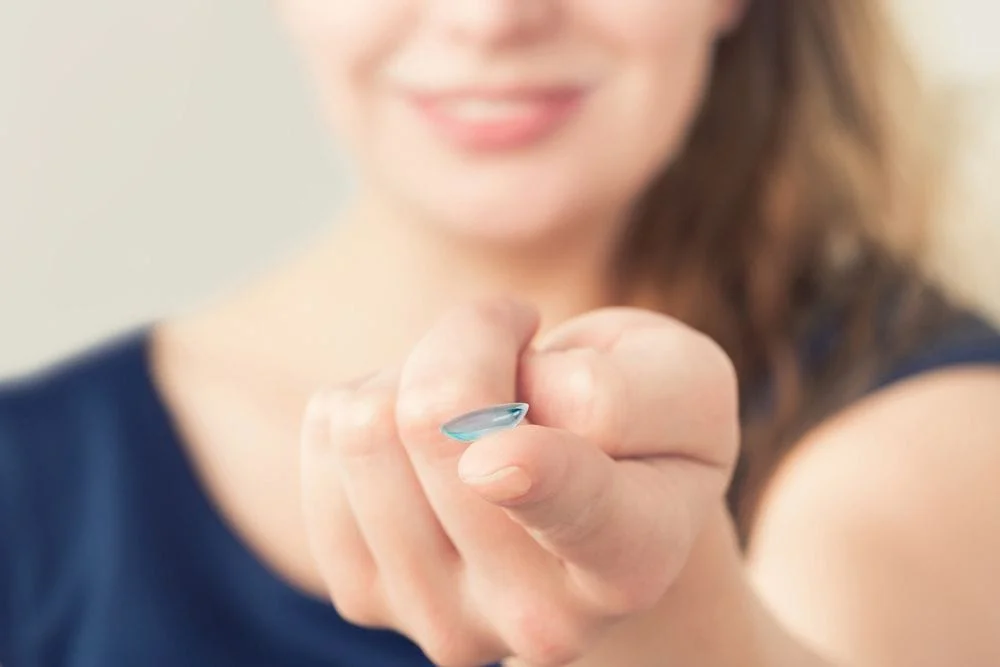 Woman holding clear contact lens and smiling