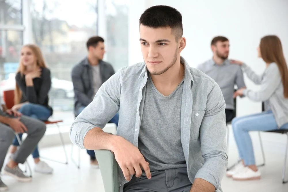Man sitting by himself in a room full of people talking to each other