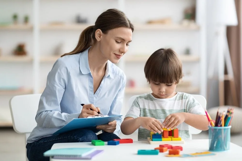 Child therapist next to a small boy, who is playing with blocks on a table