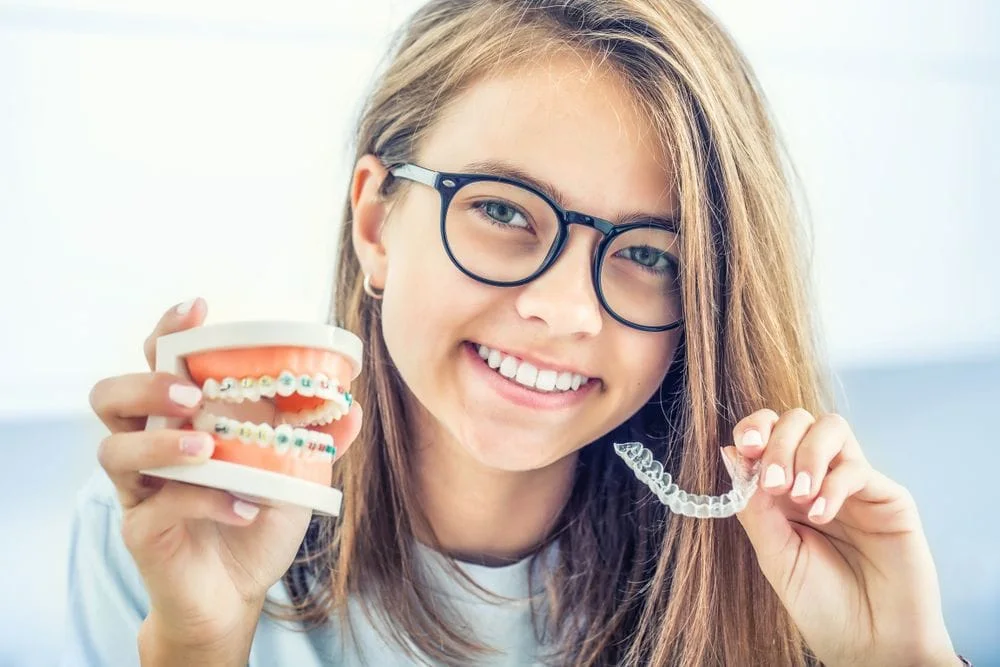 Woman smiling with model of teeth with braces and holding invisalign