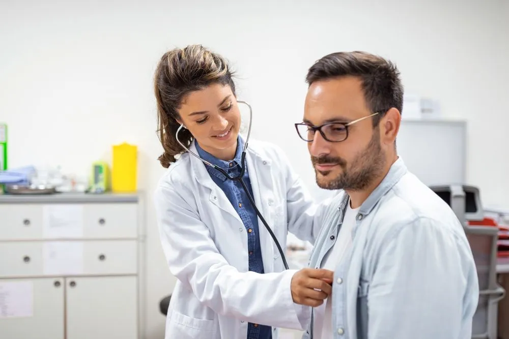 Adult in doctor's office having breathing checked by doctor using stethoscope