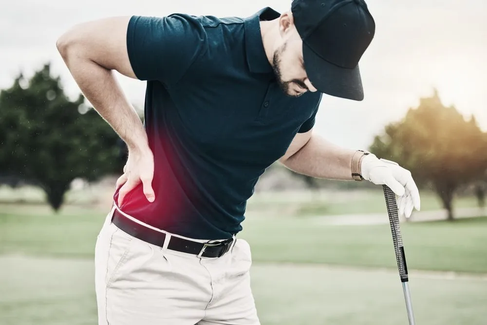 Golfer holding lower back in pain after swing, illustrating back pain during golf activity.
