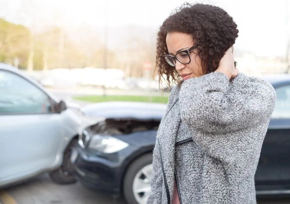 woman holding her neck in pain with an auto accident in the background